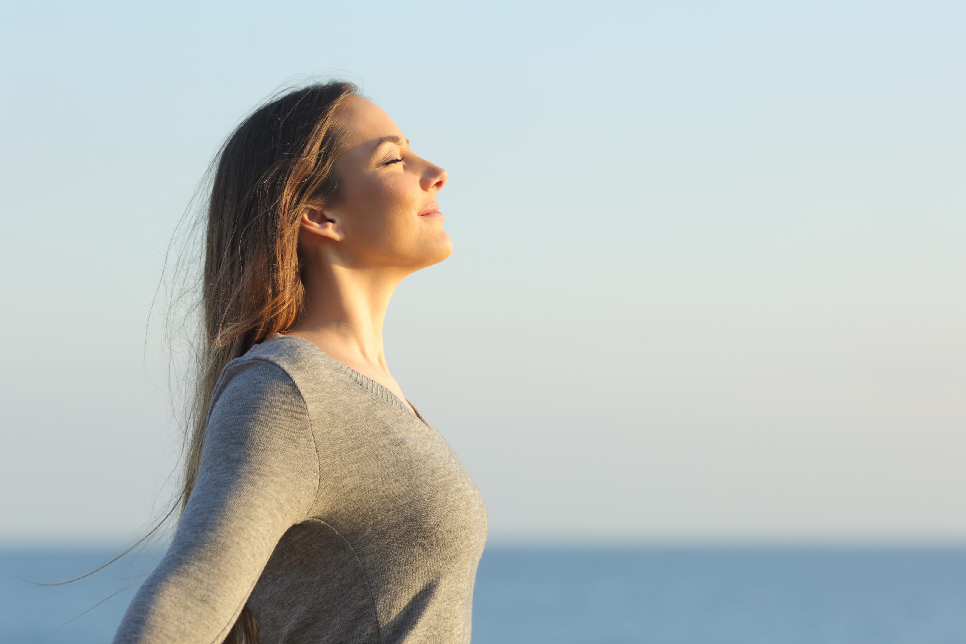 A woman is standing in the sunlight near water.